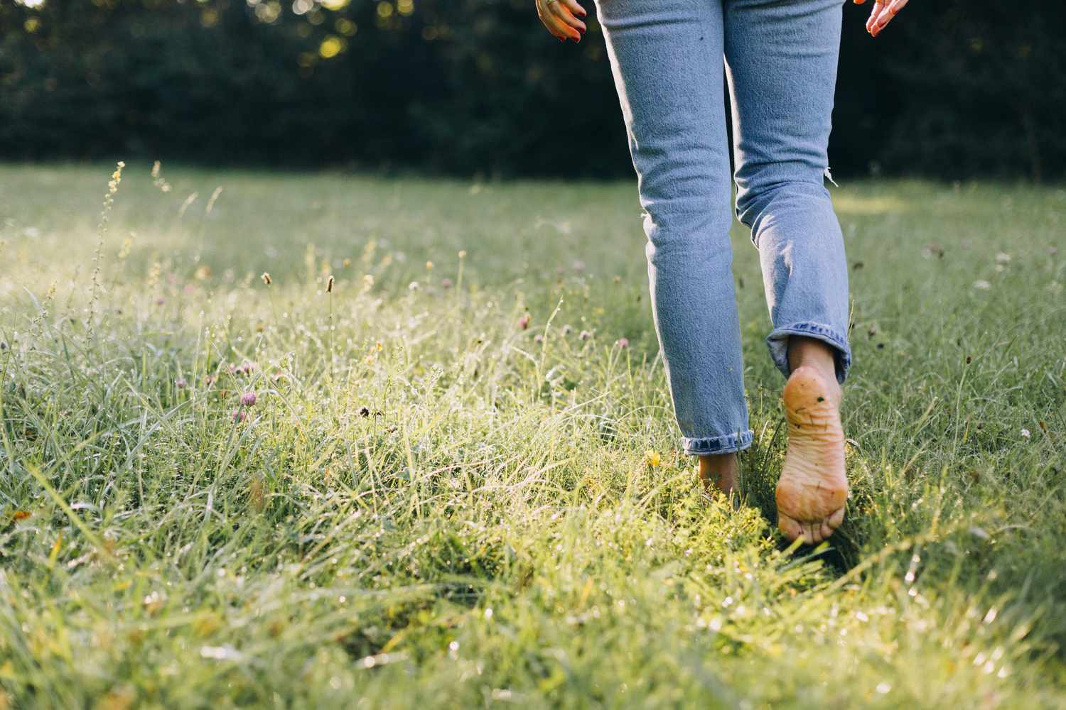 Person in jeans and barefoot walking through the grass, grounding