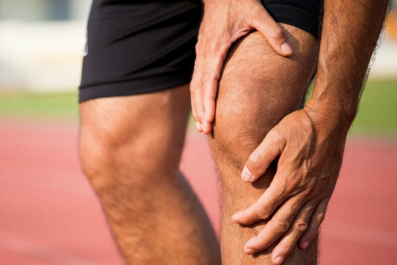 Runner holding the outside of the knee during a run, a common sign of IT band pain
